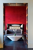 Italian designer-style hotel lobby with boat-shaped table in front of soft sofas and anthracite slate flooring contrasting with blood red wall