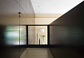 Galeriegang mit in dunkle Holzverkleidung integrierter Zimmertür und Glasbrüstung mit Blick in tieferliegendes Wohnzimmer