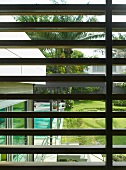 Blick durch hölzerne Sonnenschutzlamellen auf Hausecke und Palmengarten mit Pool