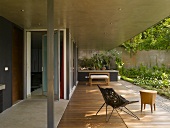 Metal armchair with fabric shell seat and side table on concrete-roofed terrace with wooden decking