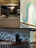 Small, set table in front of leather bench and curved, brass handrail below snaking text mural in London pizza restaurant