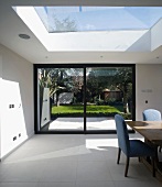 Modern house - wide sliding terrace door with view of garden and sloping skylight above sunny dining area