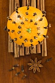 An orange pierced with cloves on cinnamon sticks