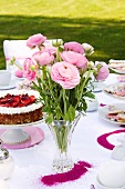 Pink ranunculus and strawberry cake on table set for afternoon tea