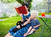 Mother and daughter sitting on lawn in garden
