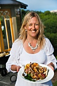 Blonde woman holding plate of grilled lamb chops, artichokes and lemons