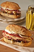 Two Muffaletta Sandwiches with Ham, Mortadella, Provolone, Mozzarella, Genoa Salami and Olive Spread; Jar of Pickles