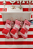 Christmas stockings hanging from bracket shelf on red and white striped wall