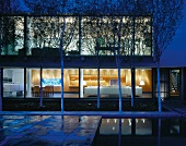 Courtyard with trees in front of contemporary house at dusk with view into illuminated interior