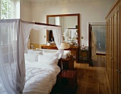 Four-poster bed with white hangings in front of bathtub and washstand in bedroom