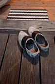 Vintage Holzpantoffeln auf Dielenboden vor offener Tür mit Türabstreifer