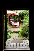 View through open front door into garden with red garden chairs below parasol