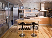 Designer kitchen with wood and stainless steel fronts; wooden table with wine rack and bar stools in centre of room