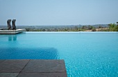Extensive infinity pool with pair of sculptures and view of distant landscape