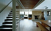 Open-plan living space with dining table, fireplace and staircase separated by glass wall