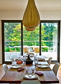 Ballonartige Hängelampen aus Holzstreifen über gedecktem Tisch vor Terrassentür mit Gartenblick