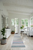 Loggia in weißem Holzhaus mit weissen Möbeln und Streifenläufer auf Dielenboden