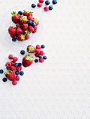 Fresh berries in a glass bowl and on a white surface