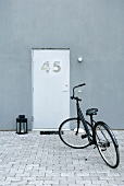 Schwarzes Fahrrad auf dem gepflasterten Vorplatz eines modernen Wohnhauses mit individueller Eingangstür
