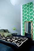 Großes Doppelbett mit floraler Tagesdecke und antiker Spiegel vor Tapetenstreifen mit Palmblattmotiv