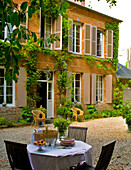 Idyllische Terrasse mit Kiesboden vor ländlichem Haus mit Fensterläden