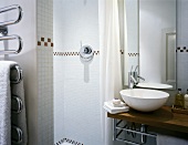 White basin on wooden surface in front of mirror in modern bathroom