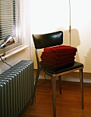 Metal chair with black leather upholstery on seat and back next to radiator painted silver-grey