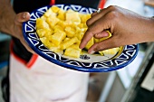 Hand nimmt Ananasstücke vom Teller