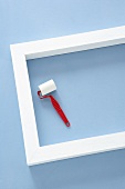 White-painted wooden frame and small paint roller on pastel blue background