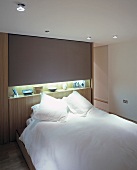 Double bed with snow-white linen in front of wall unit with indirect lighting and knick-knacks