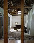 View through half-open glass door into historic attic room with antique upholstered furniture and dresser; pebbles and terracotta tiles on floor