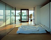 Modernes Schlafzimmer im japanischen Stil mit Futon auf Tatami-Matten und Blick auf japanischen Terrassengarten vor Stadtkulisse