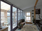 Teppich mit grafischem Tiermotiv vor Ledersofa und Holzmöbel im einfachen, skandinavischen Stil in Wohnzimmer und Wintergarten