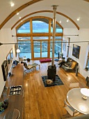 Open-plan living space seen from above with central wood-burning stove below arched ceiling and glass wall with view of wooden terrace