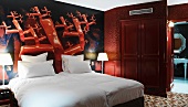 Plakative Wandbemalung in Knallrot hinter blütenweissem Bett in Hotelzimmer mit Bad ensuite