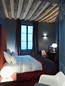 Double bed with red header in French hotel room with dark decor and exposed ceiling beams