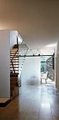 Frosted glass partition between flight of wooden stairs and perforated sheet metal spiral staircase in contemporary house