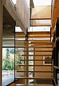 Pared-down stair structure with open treads fixed on glass wall in open-plan living space of modern wooden house