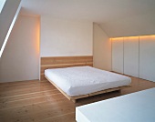 Simple bedroom with mattress on wooden platform in white attic room with indirect lighting
