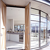 Open-plan kitchen with white furniture and a view of the city through floor-to-ceiling windows