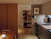 A modern living room-cum-kitchen with a view of a neighbouring room and a bookshelf