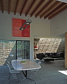 View from dining area with wooden beams on ceiling to living space with black leather couch and brick wall