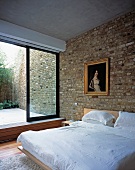 A modern bedroom with brick walls, an antique painting in a gold frame and view into a courtyard