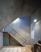 Schlafzimmer mit Wänden und schräger Decke aus Beton und mit einer Betontreppe