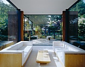 weiße Polstersofagarnitur im modernen verglasten Wohnraum und Gartenblick