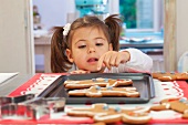 A little girl looking over a the edge of a table at gingerbread men on a baking tray