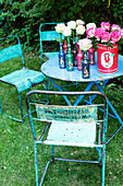 Retro garden table with roses in bottle vases and old metal chairs