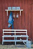 White garden bench with cushions, shelf, watering can and red wooden wall