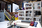 Living area with white furniture in brick loft with reclaimed staircase leading to higher level