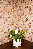 Flowerpot with plastic plant on table against floral wallpaper